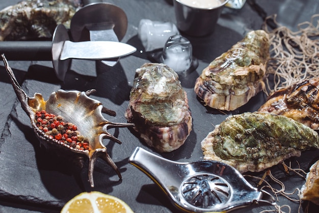 Oysters on stone plate with ice, lemon, fishing net, pepper and knife.