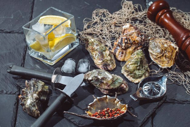 Oysters on stone plate with ice, lemon, fishing net, pepper and knife.