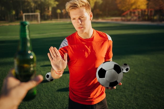 oyung player showing stop sign to human that offers him bottle of alcohol