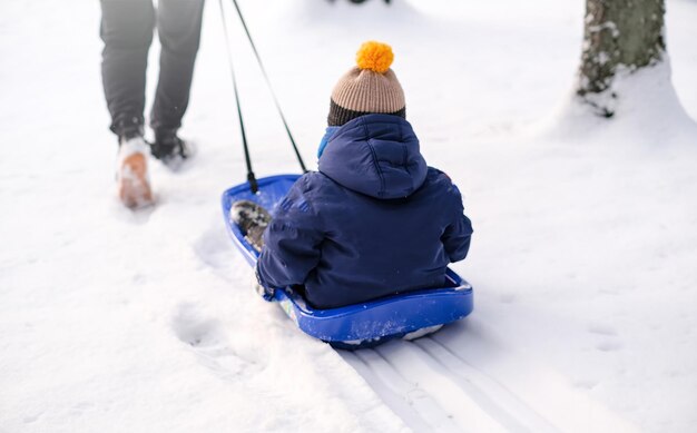 Pa neemt zijn zoon mee op een slee door de sneeuw in het park.