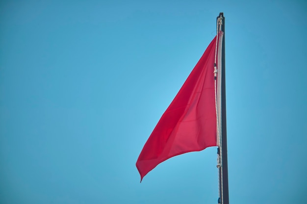 Paal met verhoogde rode vlag, symbool van gevaar voor zwemmers en navigators.