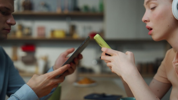 Paar dat gadgets gebruikt die afzonderlijk van muziek in hoofdtelefoons genieten bij close-up van de keuken