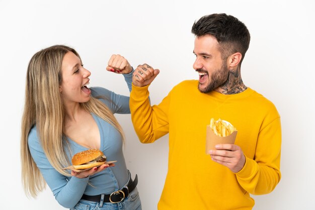 Paar dat hamburger en gefrituurde chips houdt over geïsoleerde witte achtergrond en een overwinning viert in winnaarspositie