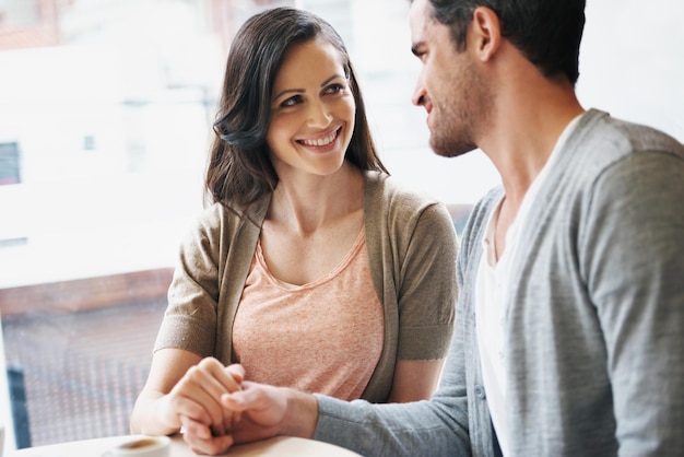 Paar dat handen vasthoudt en liefde op een date in een café restaurant en koffieshop voor verbinding binding en zorg Vriendin vriend of geliefden met genegenheid glimlach of gelukkig voor thee espresso of drank