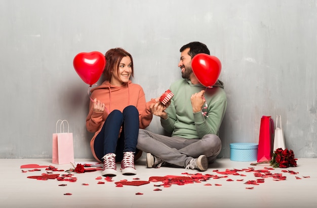 Paar dat in valentijnskaartdag een hartsymbool en ballons houdt