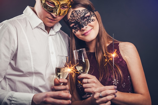 Paar dat oudejaarsavond viert die champagne drinkt en sterretjes op maskeradepartij verlicht