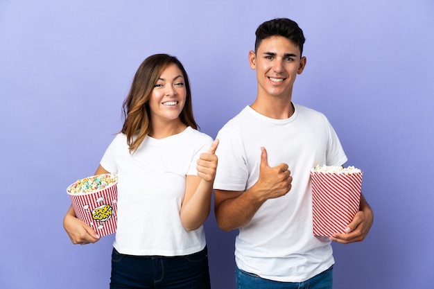 Paar dat popcorn eet tijdens het kijken naar een film op paars met een duim omhoog gebaar met beide handen en glimlachen