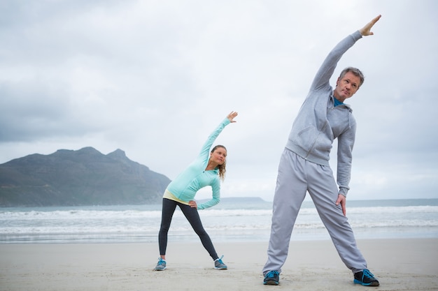 Paar dat uitrekkende oefening op strand uitvoert