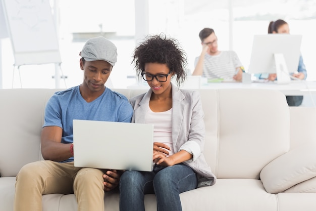 Paar die laptop met collega&#39;s op achtergrond met behulp van op creatief kantoor