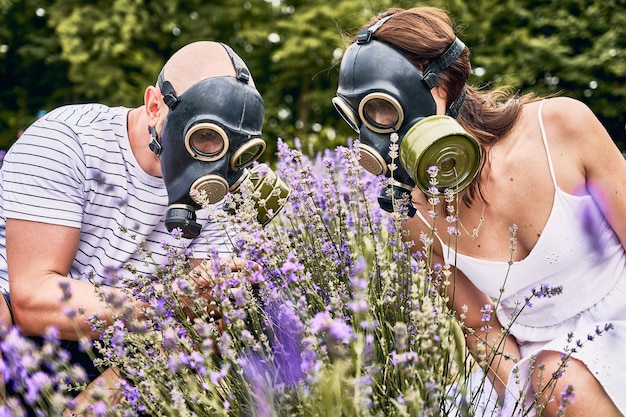 Paar gehurkt in lavendelveld met gasmaskers Bloeiende paarse bloemen wazig op de voorgrond Allergische mensen die geur proberen op te vangen door maskers