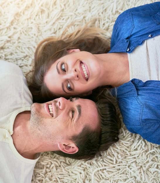 Paar gelukkig en boven op de vloer om te ontspannen in het huis met zorg grappige herinnering en binding in de woonkamer Man vrouw en komische glimlach met liggen op het tapijt met verbinding liefde en speels in het appartement