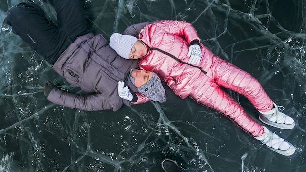 Paar heeft plezier winterwandeling tegen de achtergrond van ijs van bevroren meer Liefhebbers liggen op helder ijs met scheuren veel plezier kus en knuffel Uitzicht van bovenaf Gelukkige mensen op besneeuwd ijs Huwelijksreis liefdesverhaal