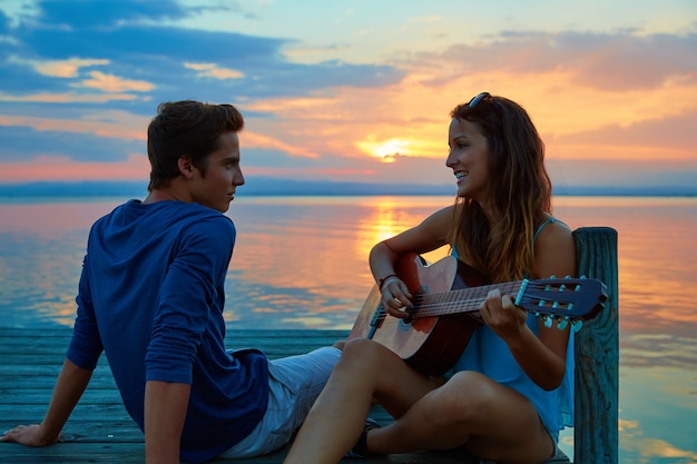 Paar het spelen gitaar in zonsondergangpijler bij schemerstrand