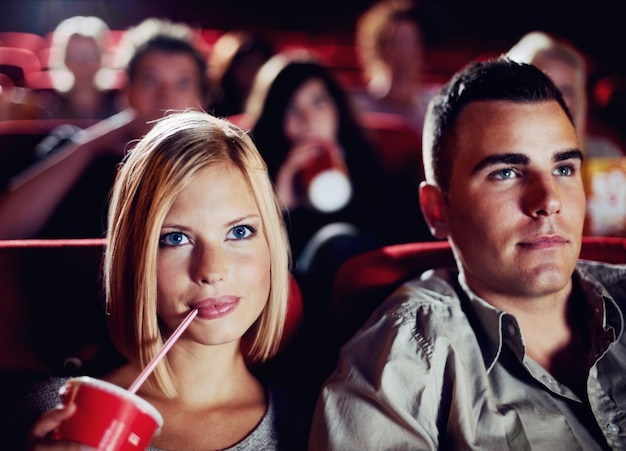 Paar in donkere bioscoop drinken cola op date in de bioscoop en man en vrouw kijken samen naar een film voor entertainment gezicht van gelukkig daten en leuk vriendje en vriendinnetje in de bioscoop