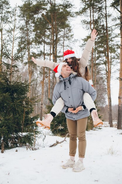 Paar in een kerstmuts en knuffelen en gek doen in een winter naaldbos