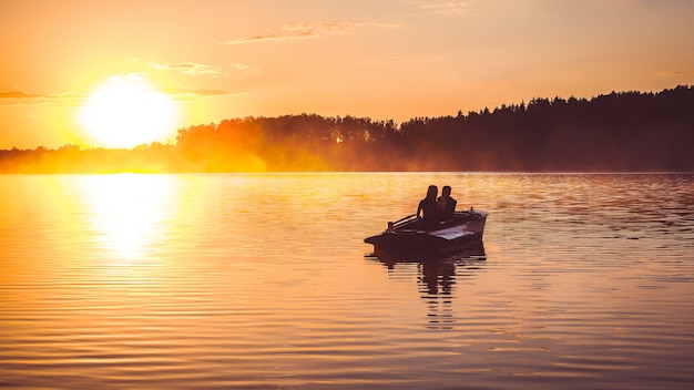 Paar in liefderit in een het roeien boot op het meer tijdens zonsondergang. Romantische zonsondergang in gouden uur.