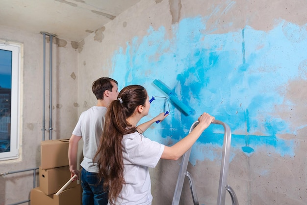 Paar in nieuw huis tijdens reparatiewerkzaamheden muur samen schilderen Gelukkig gezin met verfroller schilderij muur met blauwe kleur verf in nieuw huis Huisrenovatie DIY vernieuwen huisconcept