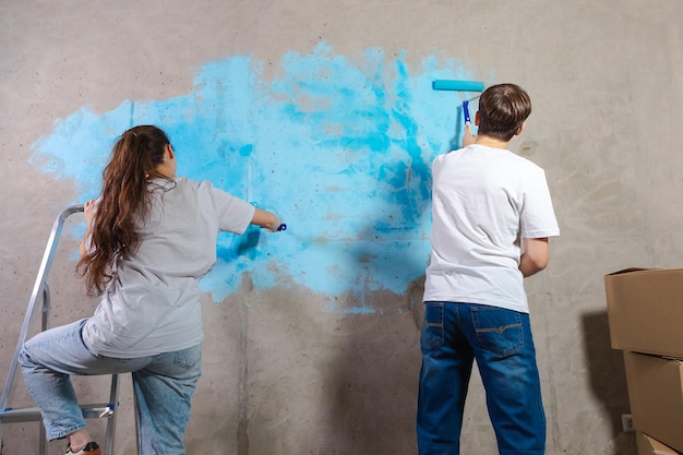 Paar in nieuw huis tijdens reparatiewerkzaamheden muur samen schilderen Gelukkig gezin met verfroller schilderij muur met blauwe kleur verf in nieuw huis Huisrenovatie DIY vernieuwen huisconcept