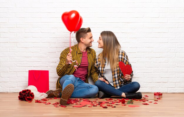 Paar in valentijnskaartdag bij binnen het houden van een hartsymbool en ballons