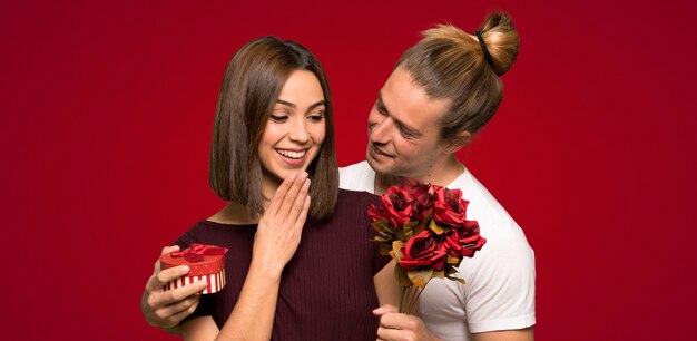 Paar in valentijnskaartdag met bloemen en giften over rode achtergrond