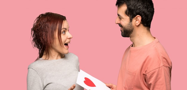 Paar in valentijnskaartdag met de kaart van de valentijnskaartendag over geïsoleerde roze achtergrond