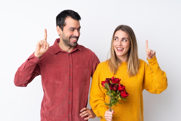 Paar in Valentine Day-holdingsbloemen over geïsoleerde muur die de oplossing willen realiseren terwijl een vinger opheffen