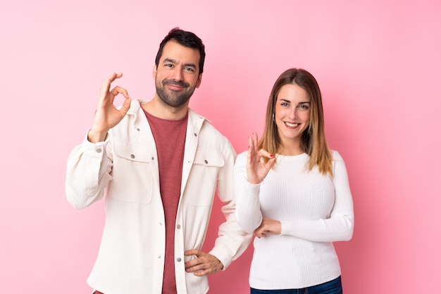 Paar in Valentine Day over geïsoleerde roze muur die een ok teken met vingers tonen