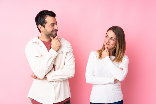 Paar in Valentine Day over geïsoleerde roze muur die elkaar bekijkt