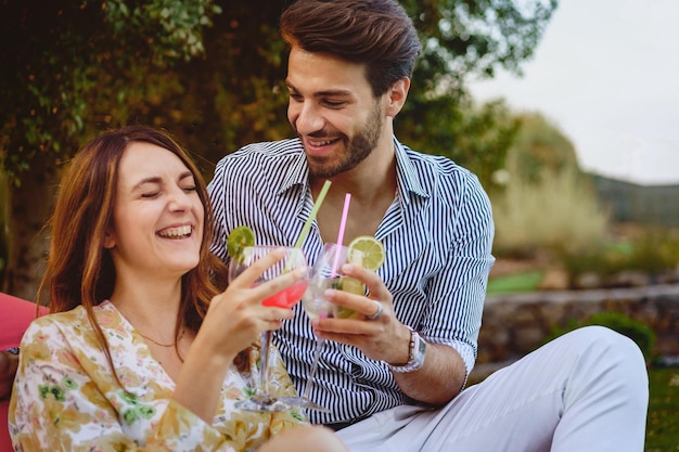 Paar jonge mensen die plezier hebben met het roosteren van cocktailglazen die in de tuin van het luxe resort zitten