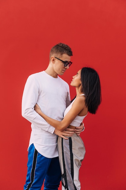 paar jonge mensen in stijlvolle vrijetijdskleding knuffelen tegen de achtergrond van een rode muur