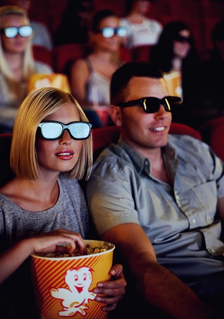 Paar kijken samen naar een film in een bioscoop met een 3D-bril terwijl ze popcorn of een snack eten Jonge man en vrouw zitten kijken naar een actiefilm of film voor entertainment tijdens een date in een theater