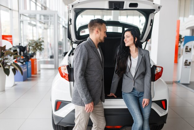 Paar kopen nieuwe auto in showroom, man en vrouw in de buurt van de geopende kofferbak.