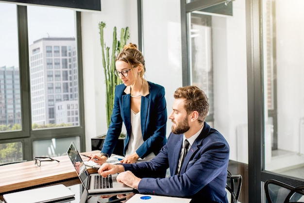 Paar managers in de pakken werken samen met laptop en documenten in het luxe kantoorinterieur