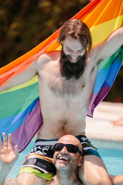 Foto paar mannen in een zwembad op elkaar spelen met een lgtb vlag