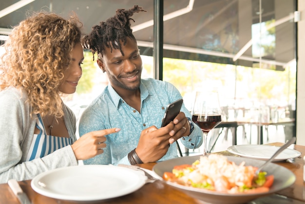 Paar met behulp van een mobiele telefoon en goede tijd samen doorbrengen tijdens een date in een restaurant.