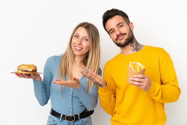 Paar met hamburger en gefrituurde chips over een geïsoleerde witte achtergrond die de handen naar de zijkant uitstrekt om uit te nodigen om te komen