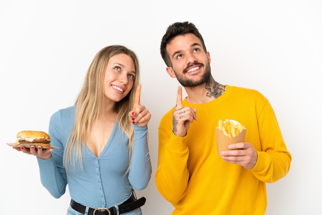 Paar met hamburger en gefrituurde chips over geïsoleerde witte achtergrond wijzend met de wijsvinger een geweldig idee