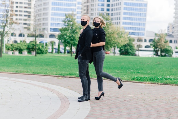 Paar modieuze beschermende maskers dragen, wandelen in de lege straat van de stad tijdens quarantaine