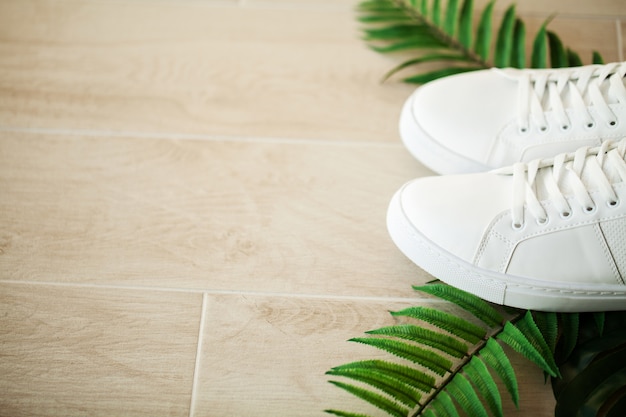 Paar nieuwe stijlvolle witte sneakers op houten vloer.