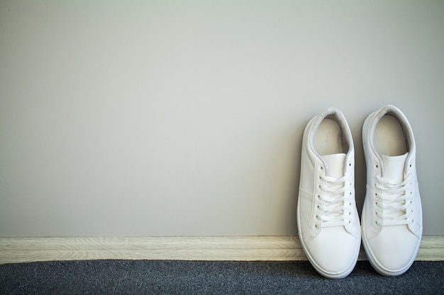 Paar nieuwe stijlvolle witte sneakers op vloer thuis