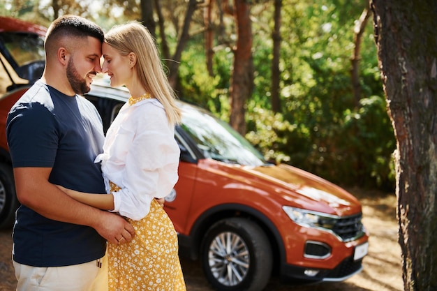 Paar omhelzen elkaar in het bos voor moderne auto.