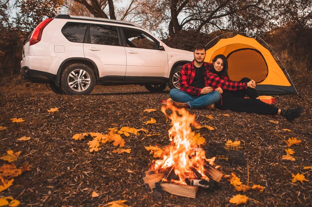 Paar op camping zitten in de buurt van vreugdevuur tent en auto op achtergrond