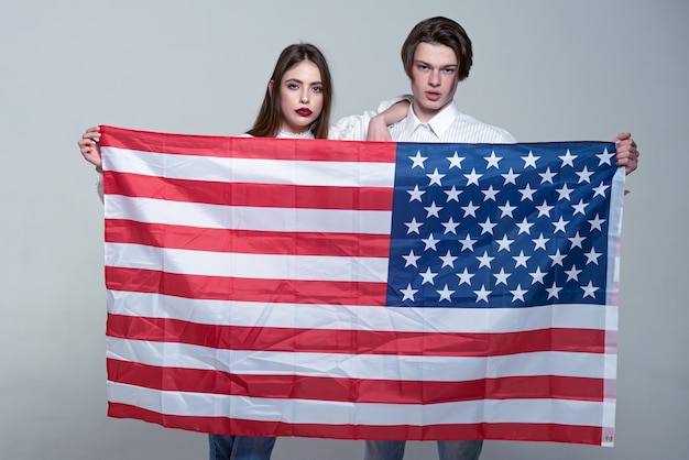 Paar op kalme gezichten houdt vlag van usa paar verwelkomt om usa te bezoeken jongen en meisje trots om amerikanen grijze achtergrond taalschool concept te zijn