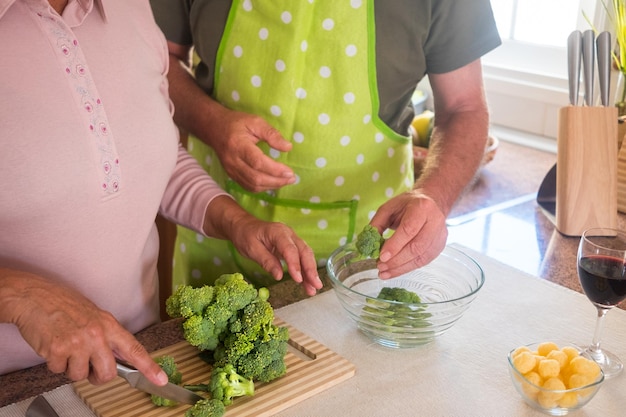 Paar oude mensenhanden die broccoli schoonmaken en snijden Twee mensen die samenwerken Gezond en vegetarisch eten Houten snijplank