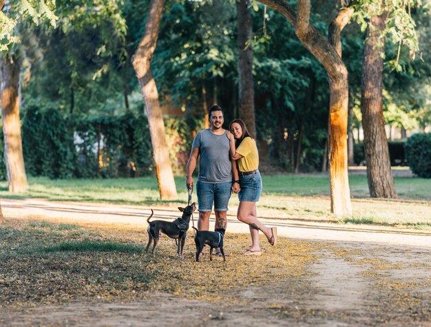 Paar poseren met hun twee honden in park. Gelukkig paar staande met zomerkleren op een zonnige dag in het park met hun twee puppy's.