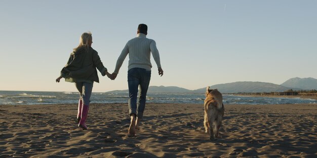 Paar rennen op het strand hand in hand met hond op herfstdag