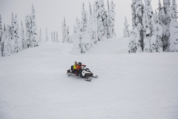 Foto paar rijdende sneeuwscooter in besneeuwde alpen
