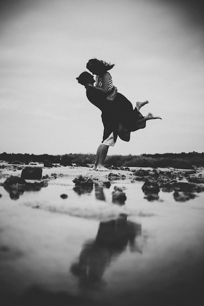 Paar ruilen knuffels vriendje tillen zijn vriendin op het strand zwart-wit foto silhouet