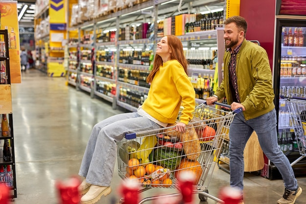 Foto paar samen winkelen in de supermarkt, man zijn roodharige vriendin dragen op kar, ze hebben plezier, genieten van tijd