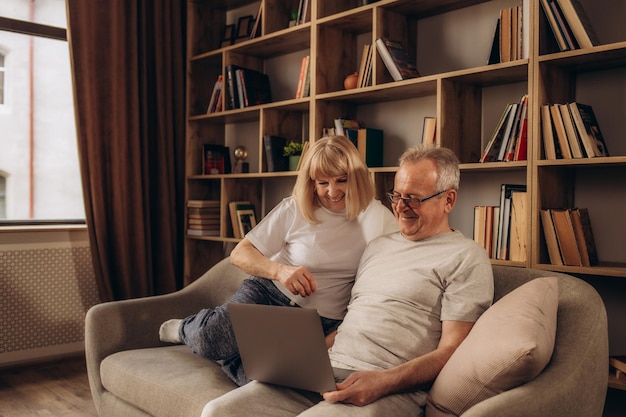 Paar senior met behulp van computer laptop op de bank thuis voor online winkelen surfen op internet